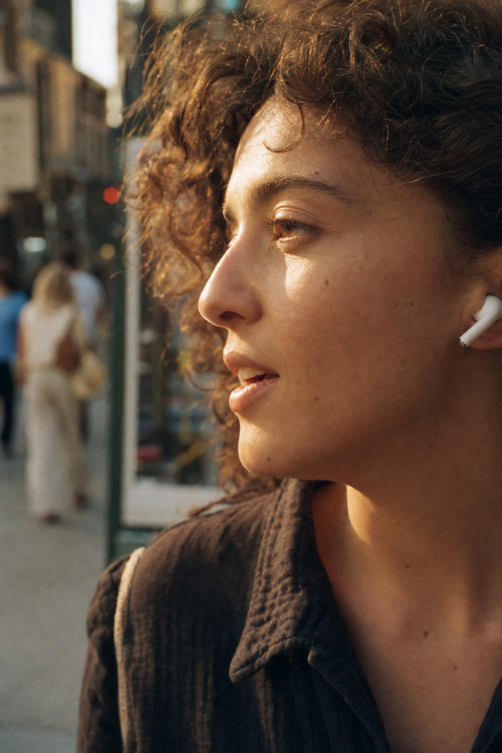 Close-up of a person whispering on a city sidewalk, in-ear buds visible.